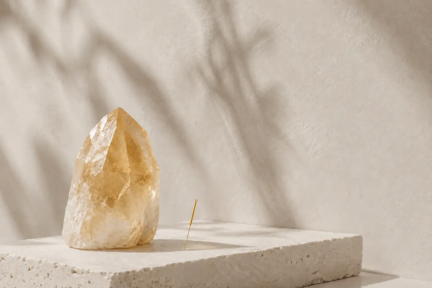 Fine gold acupuncture needle and citrine crystal on a stone plinth in soft light — facial acupuncture in Chelsea, London